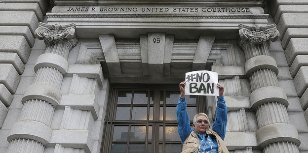 Mann mit Protestschild vor dem Eingang eines Justizgebäudes