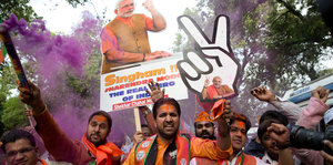 Mehrere Männer schwenken jubelnd Plakate von Indiens Premierminister Modi, sie sind in orange gekleidet