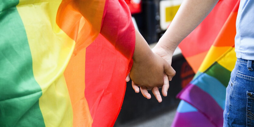 zwei Männer Hand in Hand, gehüllt in Regenbogenflaggen