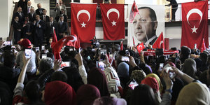 Viele Menschen stehen in einem Raum, der mit türkischen Flaggen und einem Bild des türkischen Staatschefs Erdogan behangen ist