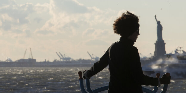 Eine Frau steht auf einem Schiff vor der Freiheitsstatue von New York