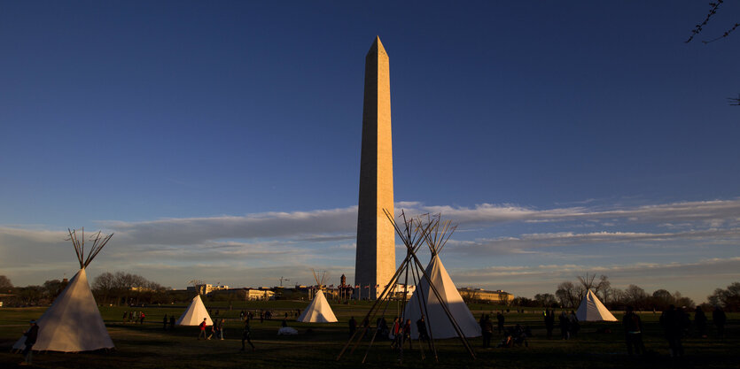 vorne Tipis, im Hindergrund eine Stadt und ein riesiger Obelisk