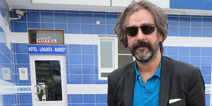 Deniz Yücel steht mit Sonnenbrille und Jacket vor einem Gebäude