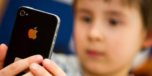 Ein kleines Kind schaut ein iPhone an.