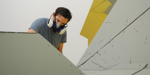 Der Künstler Florian Baudrexel arbeitet mit Schutzmaske an einem Objekt.