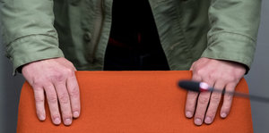 Zwei Hände halten die Rückenlehne eines orangefarbenen Stuhls
