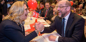 Anke Rehlinger und Martin Schulz geben sich lachend die Hand an einem langen Tisch bei einer Veranstaltung