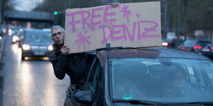 Ein Mann zeigt aus einem Auto heraus ein Schild mit der Aufschrift Free Deniz