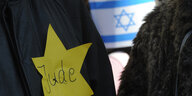 Auf schwarzen Jacken, wohl auf einer Demo. prangen einmal ein Judenstern, einmal eine Israelflagge