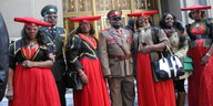 Mehrere Männer in uniformen und Frauen in traditionellen Kleidern stehen in einer Reihe