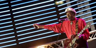 Chuck Berry im roten Hemd mit Kapitänsmütze und einer Guitarre im Arm