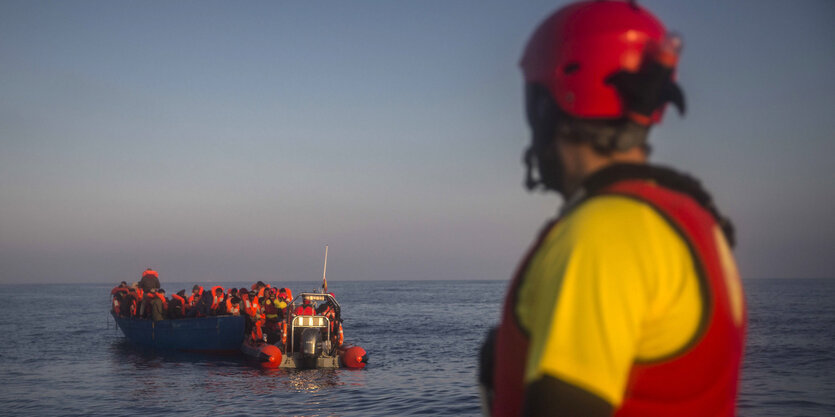 Ein Boor mit Flüchtlingen treibt vor einer Küste, beobachtet von einer NGO-Mitarbeiter