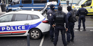 Männer in schwarzen Uniformen und Gesichtsmasken stehen am offenen Kofferraum eines Polizeiwagens