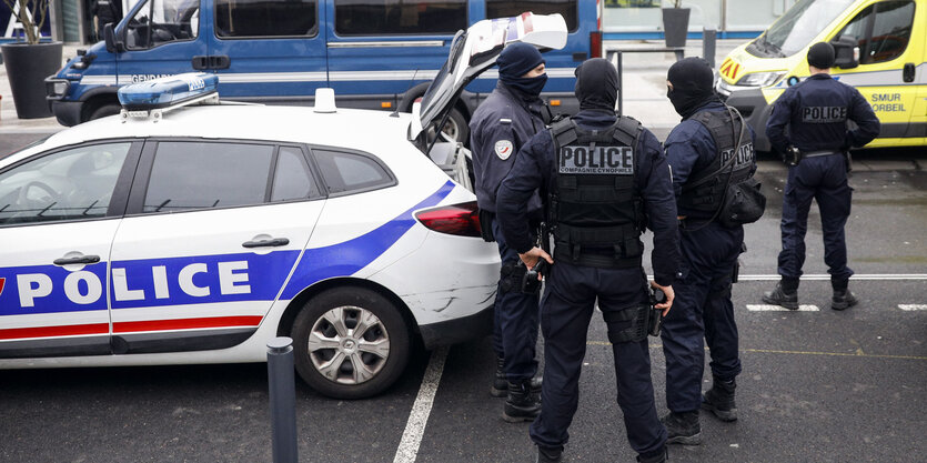 Männer in schwarzen Uniformen und Gesichtsmasken stehen am offenen Kofferraum eines Polizeiwagens