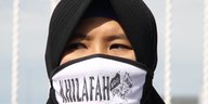 Verschleierte Frau mit Mundschutz, der die Aufschrift „Kalifat“ trägt