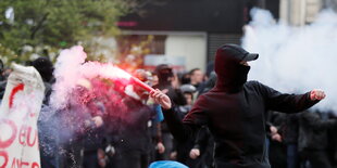 ein vermummter Mensch mit einem brennenden Bengalo in der Hand