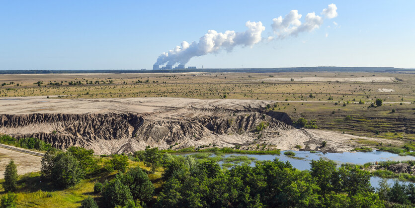 Eine kahle, sandige Landschaft, im Hintergrund rauchen Schornsteine