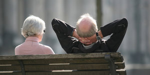 Eine Frau und ein Mann mit weißen Haaren sitzen auf einer Parkbank
