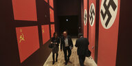 Zwischen Bannern mit Sowjet- und Hakenkreuzbannern gehen Besucher durch das Museum