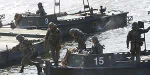 Soldaten in Uniformen auf angelegten Militärbooten, einer springt gerade vom Boot