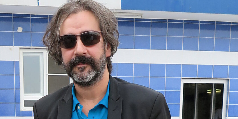 Deniz Yücel steht im himmelblauen Shirt vor einer blauen Wand - in Freiheit