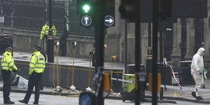 Eine Straße mit vielen Ampeln, die nicht von Autos befahren wird. Stattdessen sind Männer in gelben Warnwesten und Menschen in weißen Ganzkörperanzügen zu sehen