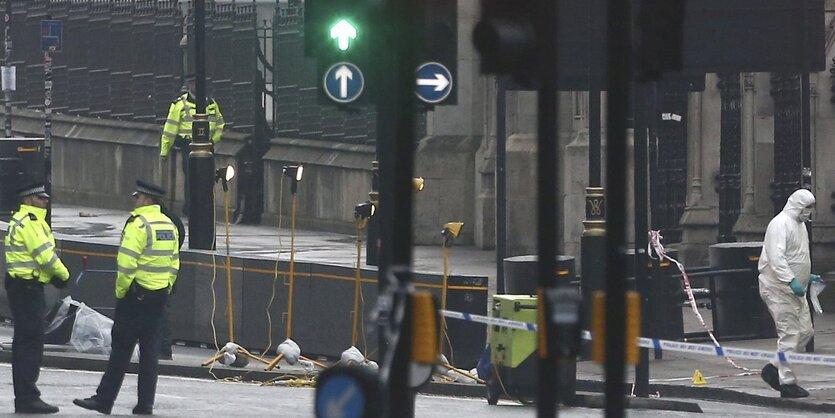 Eine Straße mit vielen Ampeln, die nicht von Autos befahren wird. Stattdessen sind Männer in gelben Warnwesten und Menschen in weißen Ganzkörperanzügen zu sehen