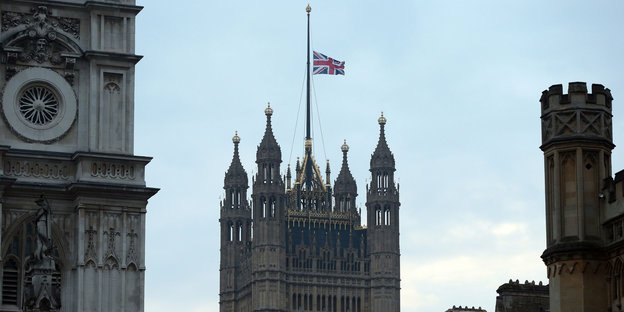 Die Spitze eines pompösen, rechteckigen Gebäudes mit der britischen Flagge darauf, die auf Halbmast weht