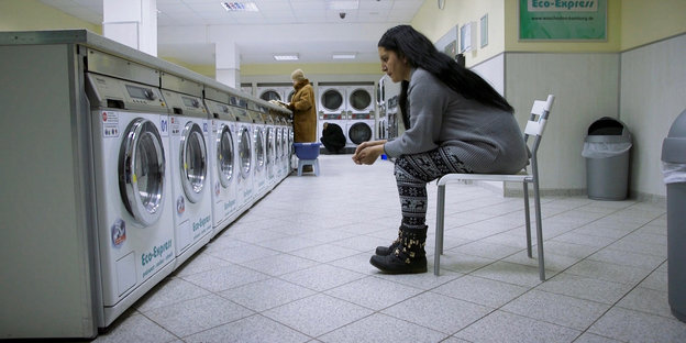 Eine Frau sitzt vor einer Reihe Waschmaschinen.