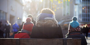 Eine Mutter sitzt zwischen ihren zwei Kindern auf einer Bank und guckt in die im Hintergrund untergehende Sonne