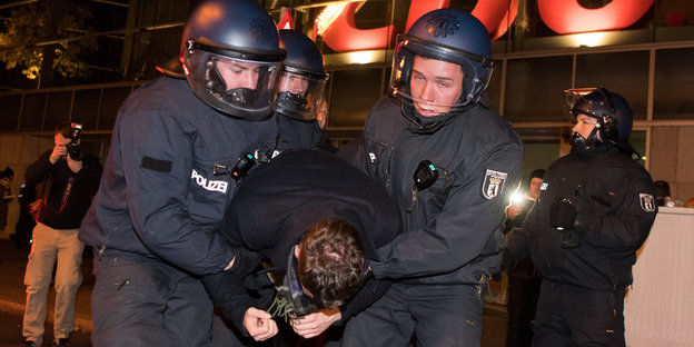 Zwei Polizisten halten einen Menschen mit Handschellen zwischen sich fest