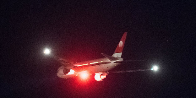 Ein Flugzeug mit roten Lichtern fliegt durch die dunkle Nacht