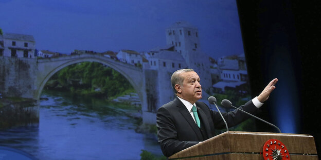 Recep Tayyip Erdoğan steht hinter einem Rednerpult und hebt den linken Arm in die Höhe