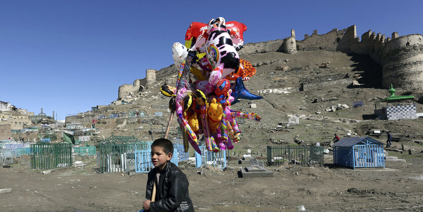 Ein junge trägt bunte Luftballons durch eine graue Landschaft