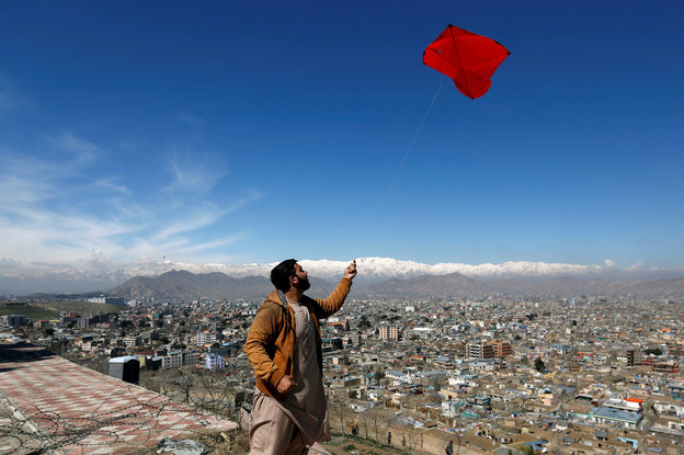 Ein Mann lässt über den Dächern einer Stadt einen roten Drachen steigen