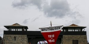Zwei Wachtüme, vor denen ein roter Wimpel weht, auf dem „Mauthausen 1938-1945“ steht