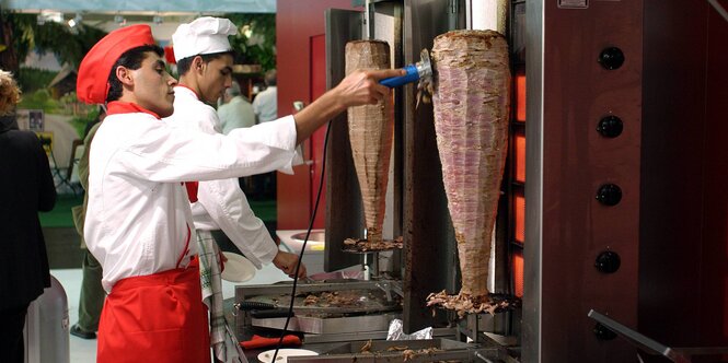 Ein Mann, der Dönerfleisch von einem Dönerspieß abschneidet