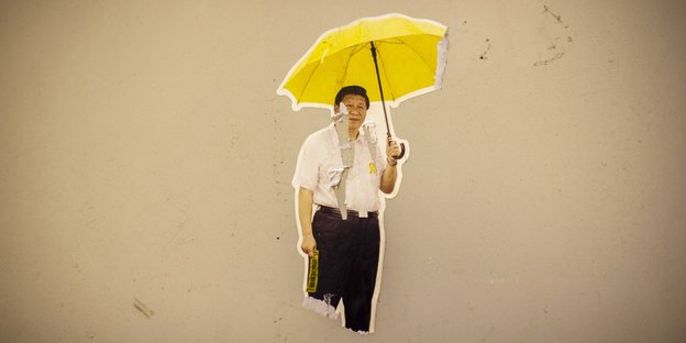 Ein Bild von Xi Jinping, der einen gelben, aufgespannten Regenschirm hält, ist an eine graue Wand geklebt