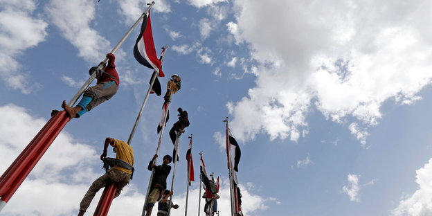Männer klettern an Stangen hoch und hissen Flaggen
