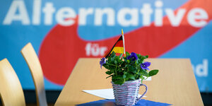 Ein Bkumenstrauß mit Deutschlandfahne im Vordergrund, dahinter AfD-Parteilogo