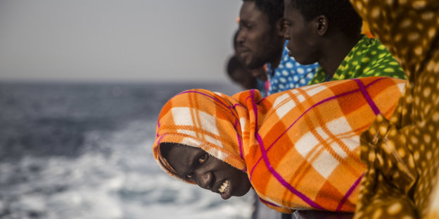 Ein Flüchtling lehnt sich, in eine Decke gehüllt, über ein Schlauchboot