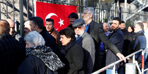 Menschen stehen vor einem Zaun mit Türkei-Flagge