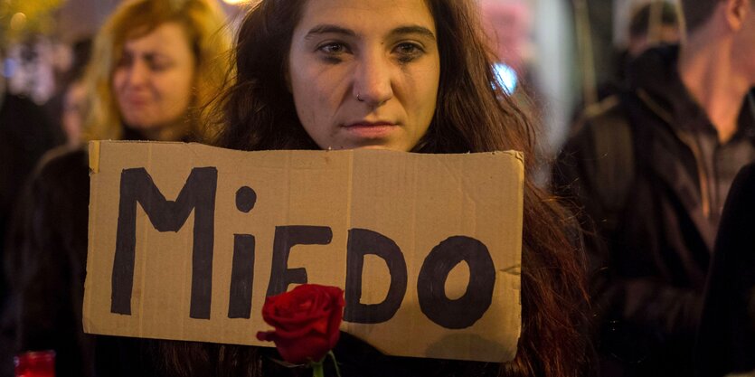 Eine Frau hält ein Schild und eine Rose in ihren Händen. Ihre Wimperntusche ist verschmiert