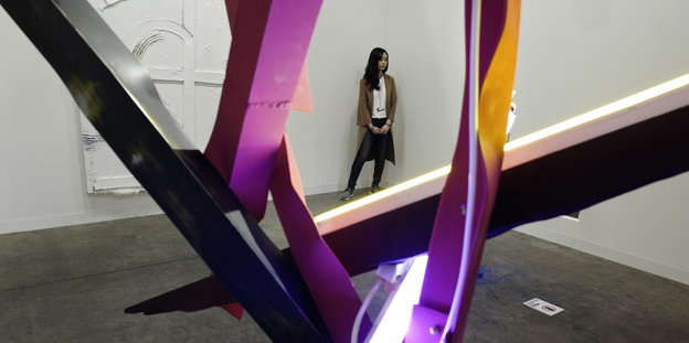 Eine junge Frau steht hinter einer verdrehten Installation aus Neonröhren und Plastikstangen