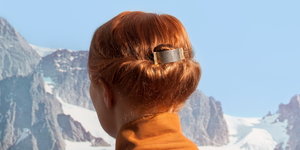 der Kopf einer rothaarigen Frau von hinten vor einer verschneiten Berglandschaft