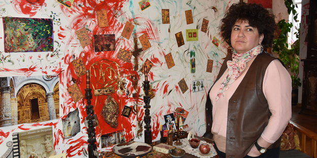 eine Frau steht vor einer bunten und mit Bildern beklebten Wand in einem Zimmer