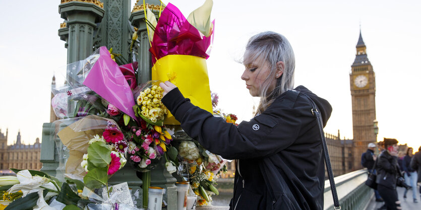 Eine junge Frau legt auf einer Straße vor dem Palace of Westminster Blumen ab