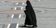 Eine ganz verschleierte Frau in schwarzer Burka läuft über einen Platz