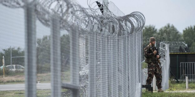 Ein Soldat patroulliert vor einem Grenzzaun aus Stacheldraht