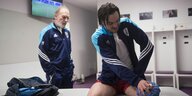 Ein Fußballspieler hält sich in einer Kabine einen Eisbeutel ans Knie, hinter ihm steht ein älterer Herr im Trainingsanzug
